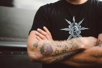 An employee stands arms folded showing culinary inspired tattoos on his arms